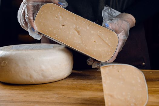 Holding goat cheese wheel and big pieces of it. Mix of cheeses from goat milk.