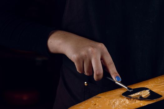 Slicing aged cheese parmesan with crystals using slicer knife. Hard cheese with knife for appetizer on dark background