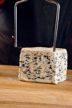 String for slicing blue cheese. Mix of cheeses on plate. Slicing dorblu, gorgonzola, roquefort. French gourmet cuisine