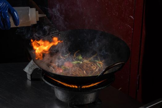 Funchoza flambe rice noodles with vegetables cooking on fire in wok pan. Street food