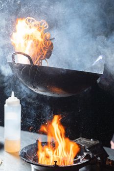 Flying flambe noodles for wok box with meat, soy sauce fried in a wok pan, street food.