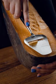 Slicing aged cheese parmesan with crystals using slicer knife. Hard cheese with knife for appetizer on dark background