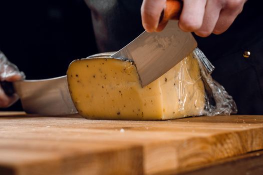 Slicing aged cheese parmesan with crystals using slicer knife. Hard cheese with knife for appetizer on dark background