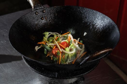 Frying vegetables in a wok pan onions, broccoli, tomatoes cherry, carrot, asparagus.