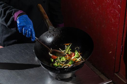 Frying vegetables in a wok pan onions, broccoli, tomatoes cherry, carrot, asparagus.