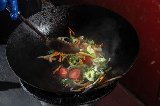 Frying vegetables in a wok pan onions, broccoli, tomatoes cherry, carrot, asparagus.