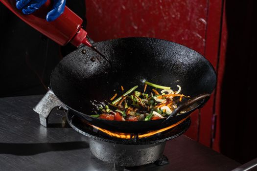 Frying vegetables in a wok pan onions, broccoli, tomatoes cherry, carrot, asparagus.