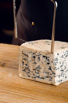 String for slicing blue cheese. Mix of cheeses on plate. Slicing dorblu, gorgonzola, roquefort. French gourmet cuisine