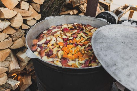 Fruit hot drink cooked in big metal can container outdoors. Field kitchen or festival food
