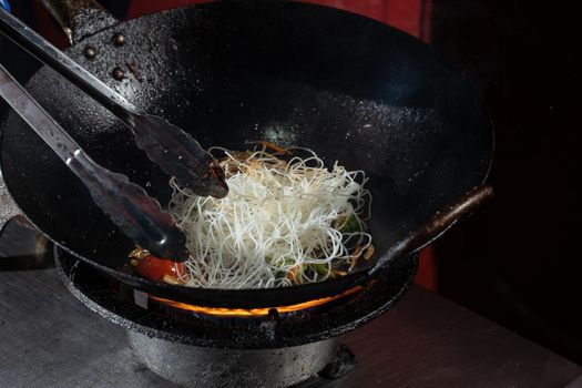 Funchoza flambe rice noodles with vegetables cooking on fire in wok pan. Street food