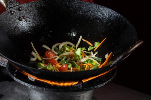 Frying vegetables in a wok pan onions, broccoli, tomatoes cherry, carrot, asparagus.