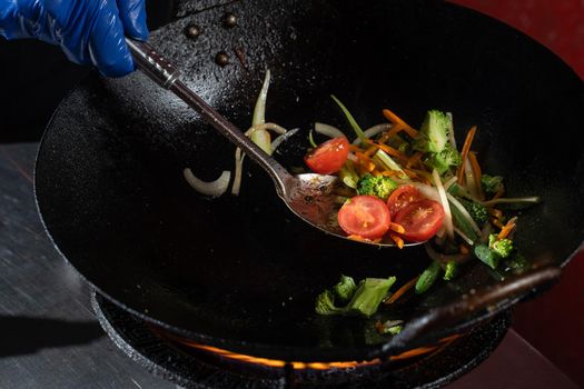 Frying vegetables in a wok pan onions, broccoli, tomatoes cherry, carrot, asparagus.