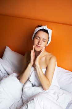 Young girl with clean skin with a towel on her head lying in bed, resting after a shower, relaxing at home