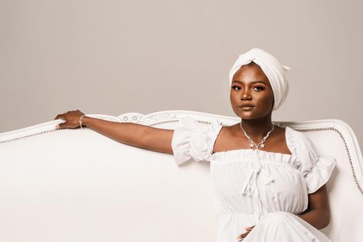 Black muslim business woman is sitting on the sofa. Confident lady weared white dress and headscarf