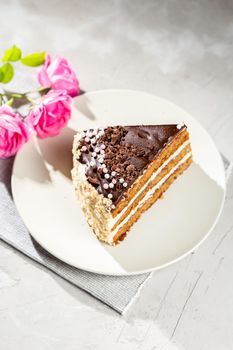 Layered cake with cream and chocolate topping and pink roses over grey background