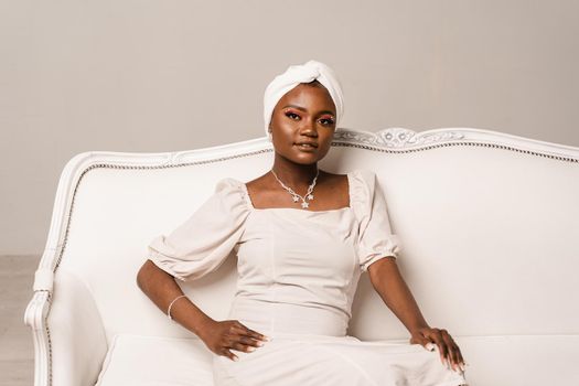 Black muslim business woman is sitting on the sofa. Confident lady weared white dress and headscarf
