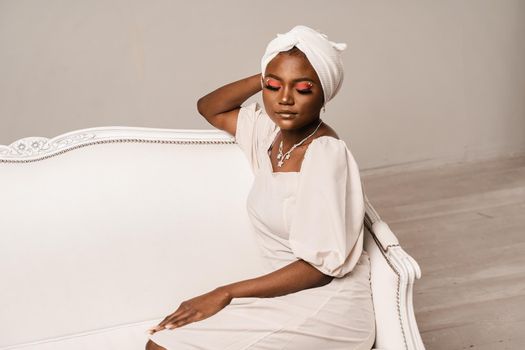 Black muslim business woman is sitting on the sofa. Confident lady weared white dress and headscarf