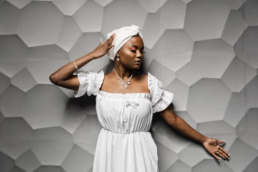 Beauty portrait of black muslim woman weared white dress and headscarf on gray background. Softness and wellness of body and skin,