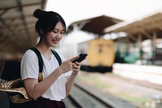 Woman waiting on station platform on background light train using smart phone. Tourist texting message and plan route of stop railway, railroad transport, booked. Enjoying travel concept.