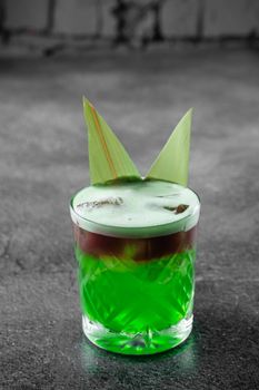 Green layered cocktail decorated with bamboo leaves on a gray background