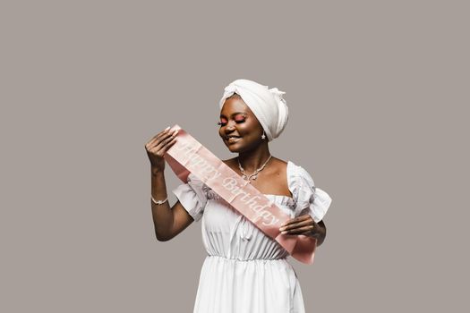 Happy muslim woman with birthday ribbon on gray background. Black african woman is celebrating her birthday