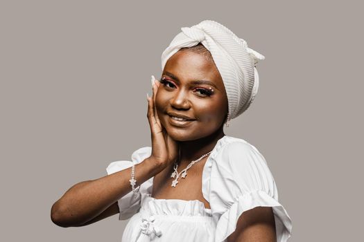 Beauty portrait of black muslim woman weared white dress and headscarf on gray background. Softness and wellness of body and skin