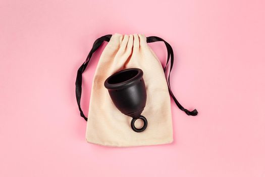 Black menstrual silicone cup on the pink background. Alternative women hygiene product