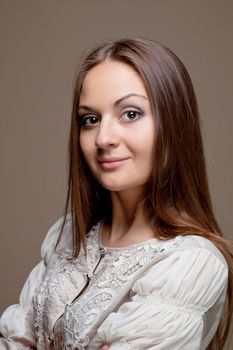 Portrait of fashionable young woman weared in light grey evening dress on biege background