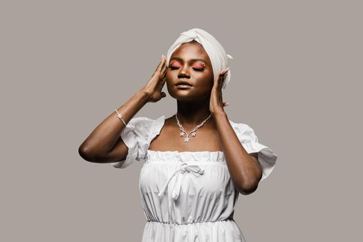 Beauty portrait of black muslim woman weared white dress and headscarf on gray background. Softness and wellness of body and skin