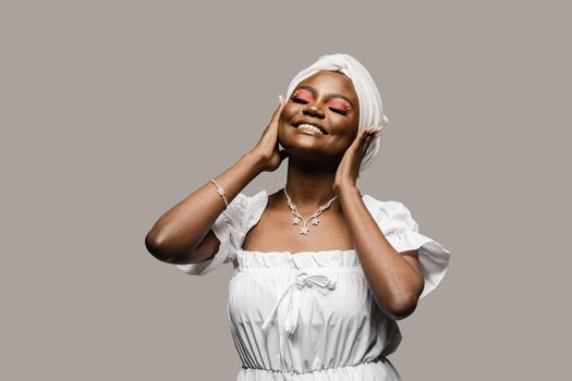 Beauty portrait of black muslim woman weared white dress and headscarf on gray background. Softness and wellness of body and skin