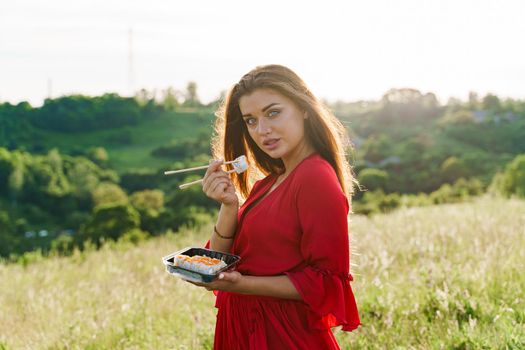 Sushi and sexy girl with blue eyes at picnic. Food delivery from japanese restaurant. Advert for social networks. Pretty girl with sushi set in 2 hand in the park.