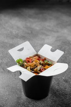 Wok in box rice noodles in black food container. Fast food delivery service. Takeaway chinese street meal