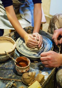 the Hands of a master and a student make a pitcher on a Potters wheel of yellow clay. Selective focus on hands