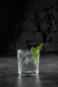 Glass with drink, ice on gray background. Alcohol cocktail decorated microgreen