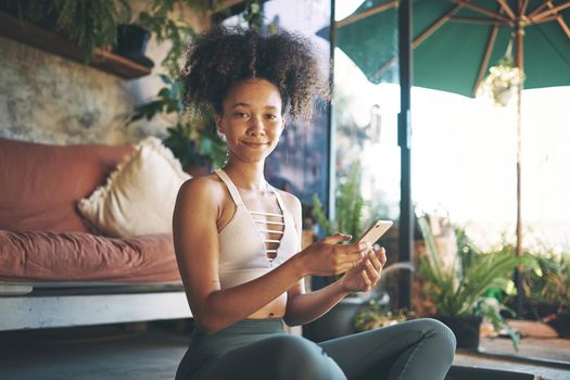 Shot of a young beautiful girl in her sportsware smiling at the camera with her phone in her hand.