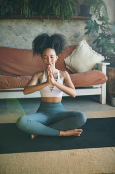 Shot of a young woman meditating in her living room - Stock Photo