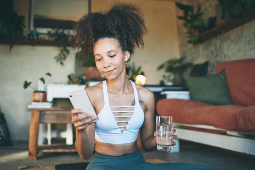Shot of a young beautiful girl in her sportswear browsing on her smartphone with water in her hand