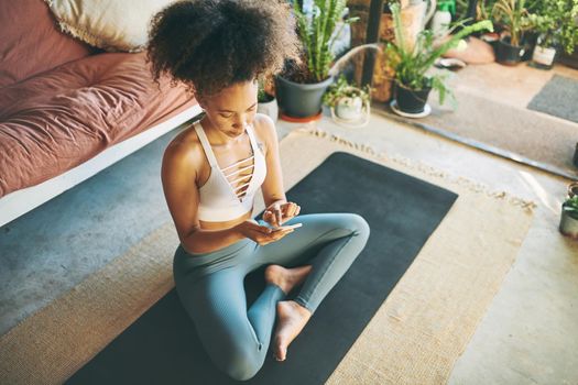 Top down shot of a sporty young woman using a cellphone while exercising at home - Stock Photo