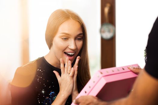 Surprised young woman opens a pink box with a present inside it