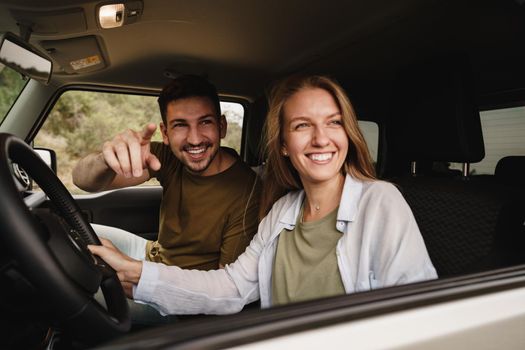 Beautiful young smiling couple sitting on front passenger seats and driving a car