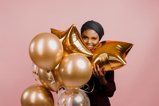 Christmas celebration. African american holiday. Attractive girl with golden helium balloons isolated peach background