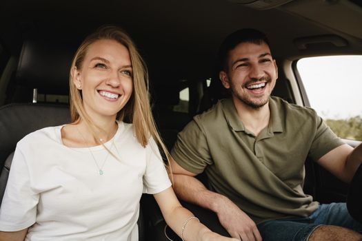 Beautiful young smiling couple sitting on front passenger seats and driving a car