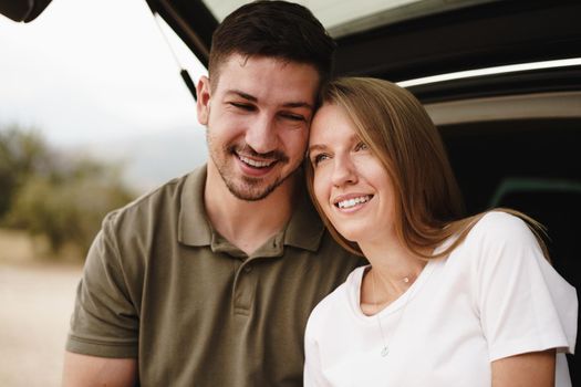 Young happy couple on a road trip sitting in car trunk outdoor