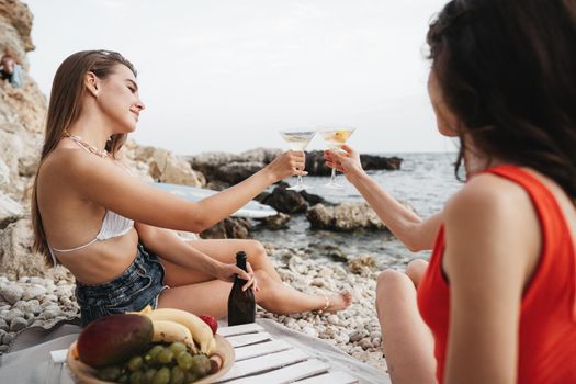 Two young female friends having a picnic on a beach drinking cocktails