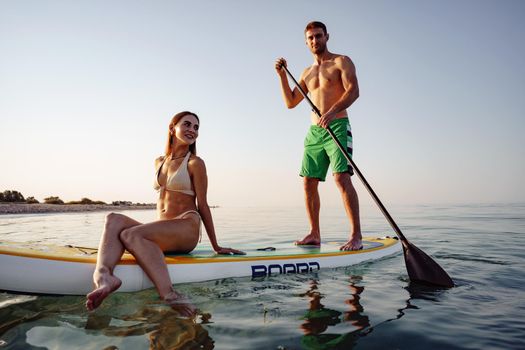 Couple of tourists young man and woman having fun paddleboarding at sea at sunset