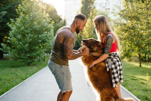 Young happy couple playing with their dog smiling in park, close up