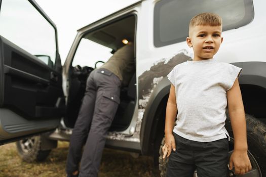 Father and little son standing near car on road trip, close up