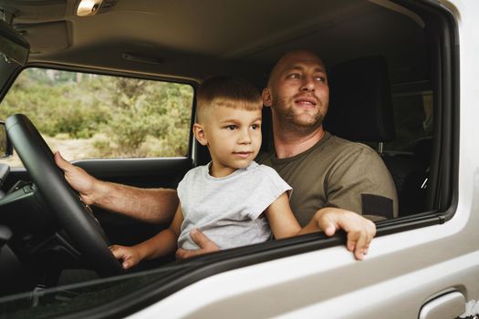 Father teaches little son to drive on road trip, close up