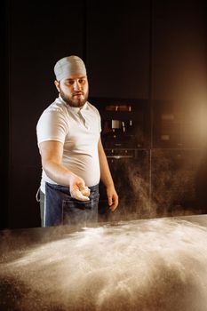 Making dough by hands at bakery or at home. Flour cloud in the air.