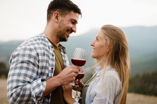 Smiling couple toasting wine glasses outdoors in mountains, close up portrait